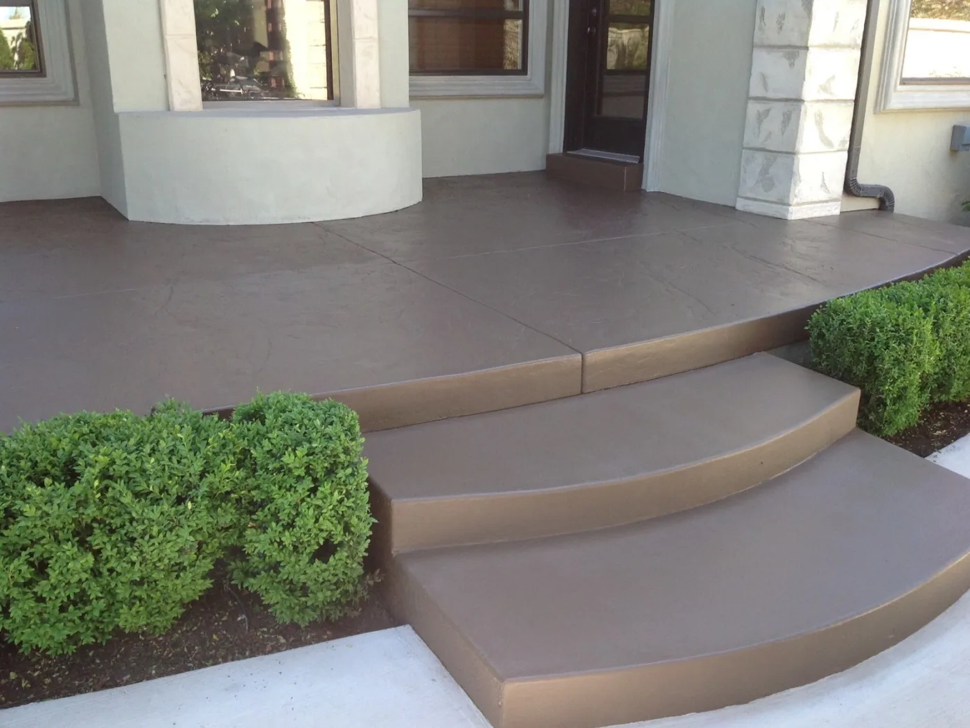 Front porch and curved concrete steps finished in a brown coating beside boxwood shrubs