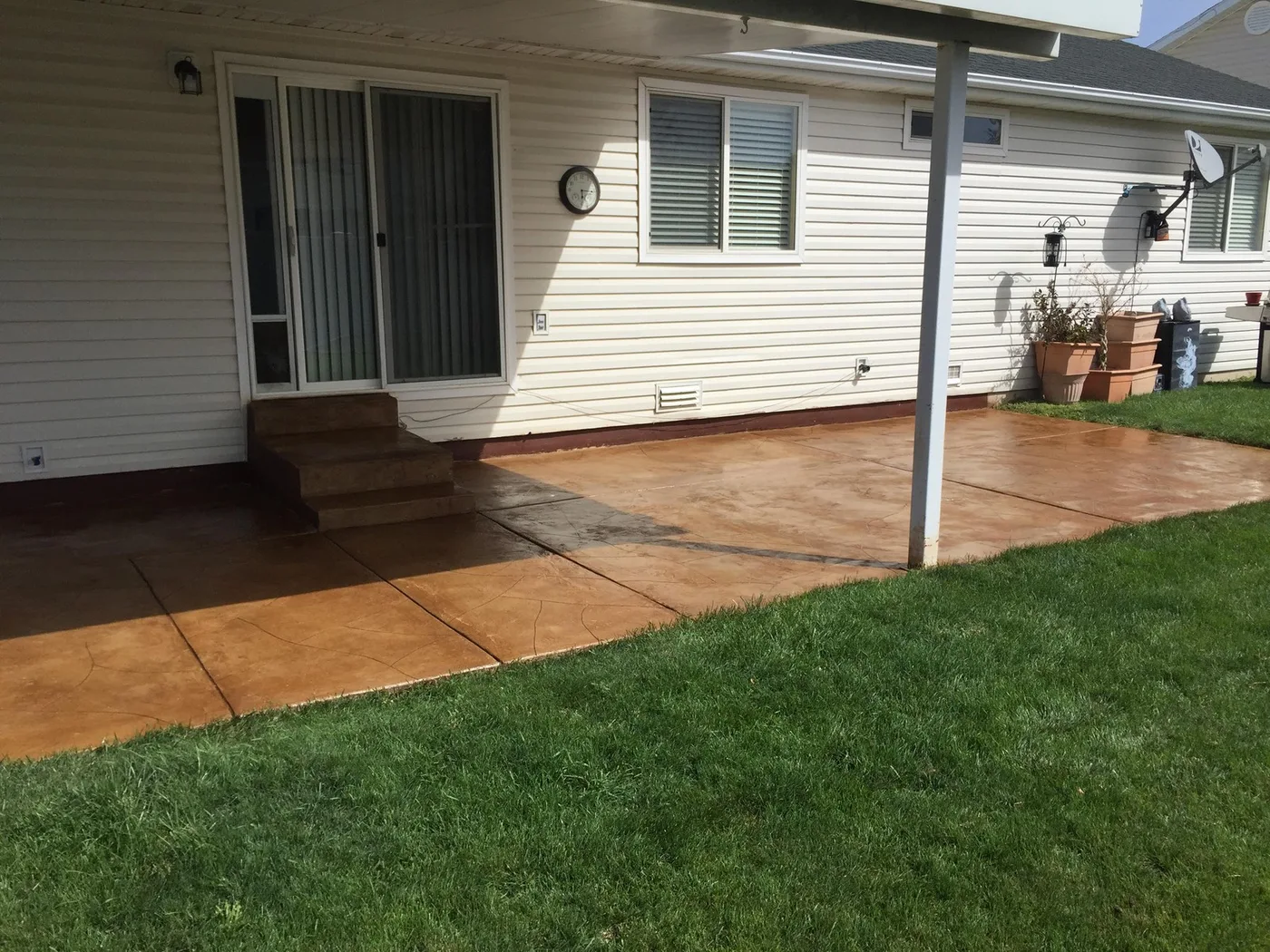 Sealed stamped concrete patio in a warm tan color behind a house